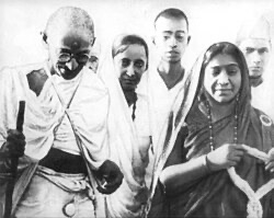 Mahatma Gandhi walking with a staff, Sarojini Naidu beside him in a bordered sari, with other figures behind them.