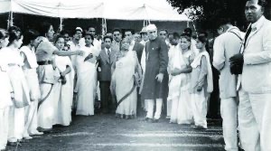A public ceremony photographed from a distance: a crowd of people in white clothing gathered under an awning around a group of officials.